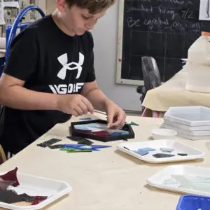 Boy creating mosaic art in a classroom.