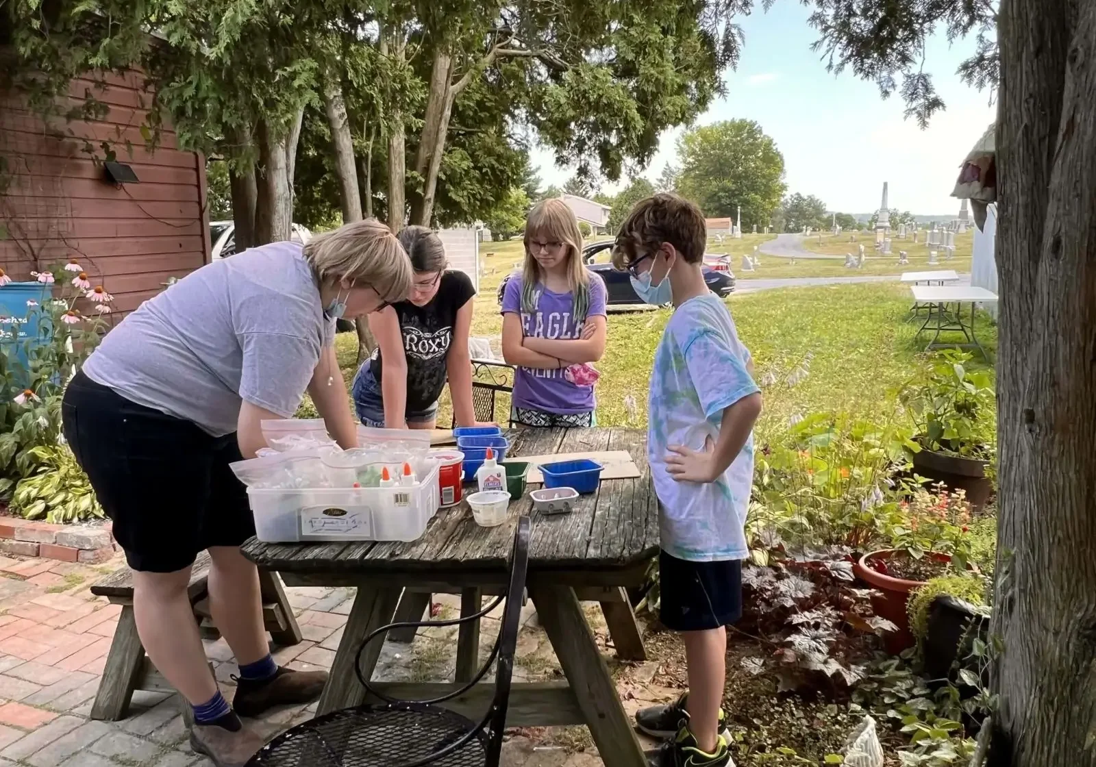 Children and adult crafting outdoors at table.